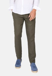 Olivově zelené lněné kalhoty se střihovým designem rovného nohavice, s texturovanou tkaninou a uvolněným střihem. Doplněné modrými semišovými botami.