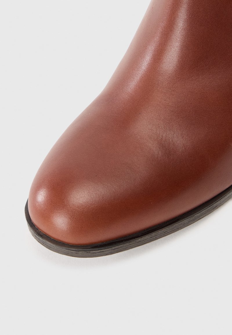 Bottines en cuir marron avec un bout arrondi, texture lisse et semelle plate noire. Des coutures sont visibles le long du côté.