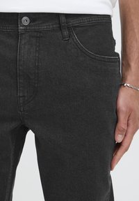 Jeansi din denim gri închis, cu croială clasică, design cu cinci buzunare, închidere cu nasture metalic și textură ușoară în material.