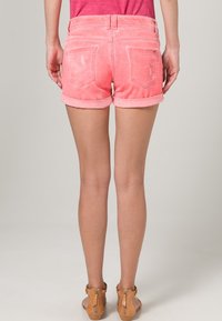 Rosa denimshorts med uppvikta muddar, två bakfickor och en mjuk textur. Bärs med bruna sandaler mot en neutral bakgrund.