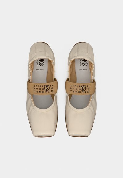 Μπεζ παπούτσια από μαλακό ύφασμα σε στιλ Mary Jane με ελαστικό άνοιγμα και καφέ λουράκι αποτυπωμένο με αριθμούς και έναν κύκλο γύρω από το 6, εμφανιζόμενα από πάνω.