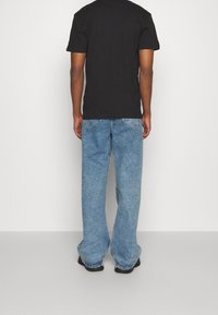 Svart bomulls t-shirt i kombination med löst sittande, ljusblå denimjeans. Jeans har en urtvättad textur och standard fickdesign.