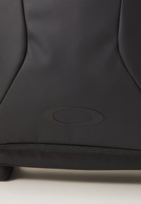 Black backpack made from textured material featuring a smooth zipper and a prominent oval logo on the front.