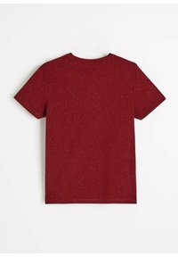 Czerwona koszulka z krótkim rękawem wykonana z miękkiego materiału o drobnoziarnistej fakturze. Tył ma dekolt w serek i wykończone brzegi.