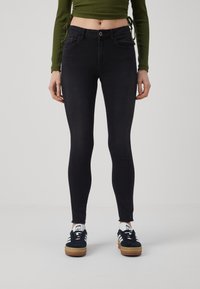 Svarta skinny jeans med hög midja, med framfickor, knappstängning och fransad fåll. Bärs med mörka sneakers.