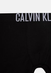 Sorte bomullsboxere med bred elastisk midjebånd som har "CALVIN KLEIN" logo i grått, glatt tekstur og tettsittende design.