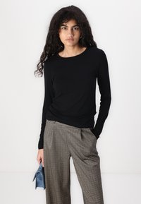 Fekete, hosszú ujjú felső, kerek nyakkivágással, kockás, bő szárú nadrággal és egy kicsi kék kézi táskával párosítva. Sima anyagú textúra.