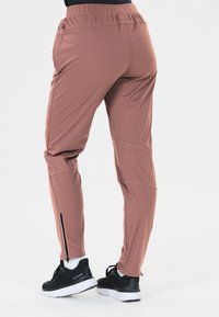 Roze sportbroek met een taperend ontwerp, elastische tailleband en ritsen bij de enkels, gecombineerd met zwarte sneakers.