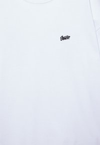 Biely textil s malým čiernym vyšívaným nápisom "SNIP" v hornej ľavej časti.