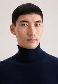 Pull à col roulé marine en tricot doux, avec un col haut et des détails côtelés, présenté sur un fond neutre.