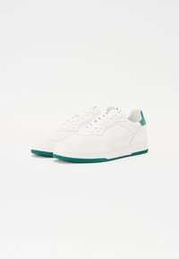 Hvite sneakers med en teksturert overflate, grønne detaljer på hælen og sålen, samt perforerte detaljer på sidene. Klassisk snøring.