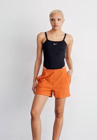 Svart atletisk bodysuit med tunna remmar, tillsammans med orange ruggade shorts med fickor. Båda plaggen har minimal märkning.