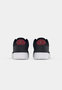 Une paire de baskets noires et bordeaux avec des semelles blanches vue de l'arrière sur un fond blanc uni.