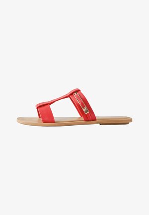 Flache Sandale mit beigefarbener Sohle und zwei roten Riemen, einer mit goldfarbenem rechteckigem Schnallendetail, seitlich auf weißem Hintergrund gesehen.