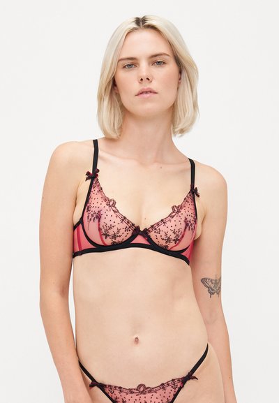 Soutien-gorge rose transparent avec broderie florale noire, bonnets en triangle, fines bretelles et accents noirs. Comprend de petits nœuds décoratifs sur les bretelles.