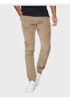 Beige Cordhose mit elastischem Bund und Kordelzug, im schmal zulaufenden Schnitt und mit Seitentaschen, kombiniert mit weißen Sneakers.