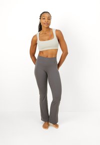 Pantalones de yoga grises acampanados combinados con un sujetador deportivo de escote cuadrado en gris claro. El atuendo presenta una textura suave y un diseño ajustado.