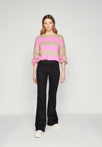 Virkat tröja i beige med rosa horisontella ränder, kombinerad med svarta utsvängda byxor och vita sneakers. Avslappnad passform och rullade ärmar synliga.