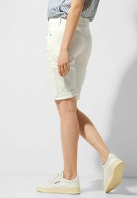 Białe szorty dżinsowe z podwiniętym dołem i wieloma kieszeniami, w połączeniu z niskimi kremowymi trampkami z teksturowanym wykończeniem i logo.