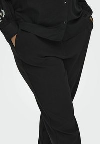 Melnas bikses ar brīvu piegriezumu, ar sānu kabatām, gludu tekstūru un vissvarīgākajiem šuvju akcentiem. Apvienotas ar atbilstošu melnu krekliņu.