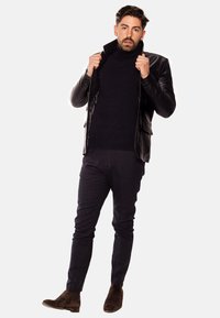 Blazer de cuero negro sobre un suéter de cuello alto de punto oscuro, combinado con pantalones oscuros a medida y botines de ante marrón.