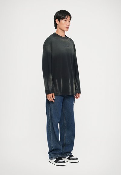 Svart langermet skjorte med en gradient-effekt, kombinert med løse blå jeans og svart-hvite sneakers. Glatt stoff, avslappet passform.