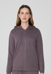 Chaqueta con capucha y cremallera en un púrpura atenuado, con un bolsillo frontal, cordón ajustable y puños elásticos. Fabricada con un tejido suave y texturizado.