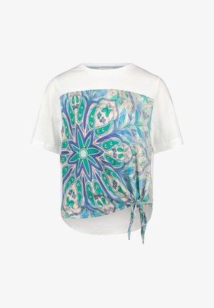 Weißes T-Shirt mit einem blauen und grünen abstrakten Print auf der Vorderseite und einem geknoteten Detail an der linken unteren Seite. Kurze Ärmel.
