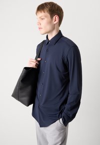 Camisa de manga larga color navy en tejido suave con cuello clásico y cierre de botones, combinada con un simple bolso tote de cuero negro.