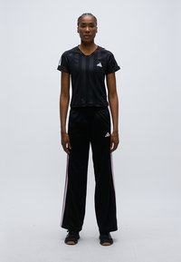 Μαύρο αθλητικό σύνολο που αποτελείται από εφαρμοστό κοντομάνικο τοπ με κάθετες ρίγες και μαύρο παντελόνι με ροζ πλευρικές ρίγες.