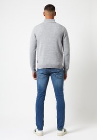Pull gris en maille avec un col montant, des poignets et un ourlet côtelés. Associé à un jean bleu et des baskets blanches avec des accents verts.