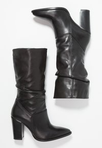 Botas de cuero negro hasta la rodilla con punta afilada y tacón bloque. Presentan un diseño holgado con una textura suave y detalles de costura mínimos.
