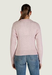 Maglione rosa a trecce con polsini e orlo a coste. Presenta una silhouette aderente e un motivo strutturato, abbinato a jeans blu.