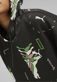 Sudadera con capucha negra que presenta patrones abstractos coloridos y logotipos de Puma. El material es suave y cuenta con un detalle de cordón texturizado en la capucha.