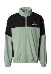 Lys grønn og svart vindjakke med høy krage, frontglidelås, elastiske mansjetter og lommer. Har logo på brystet og kontrasterende farger.