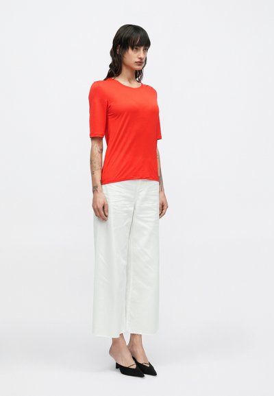 Piros, rövid ujjú felső, sima anyagból, fehér, bő szárú nadrággal és fekete, hegyes orrú magassarkú cipővel párosítva. Egyszerű dizájn.