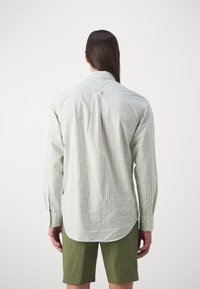 Cămașă cu mânecă lungă, în carouri verzi și albe, cu guler cu nasturi, având un bucleț atârnat în spate și manșete ajustate. Asortată cu pantaloni scurți de culoare măslinie.