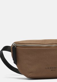 Brun tekstureret stoftalje taske med sølv lynlås og sort justerbar rem, mærket "Liebeskind Berlin" på forsiden.