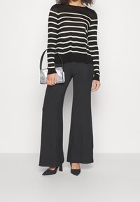 Pull rayé noir et blanc à manches longues, associé à un pantalon large noir. Sac à main rectangulaire argenté et escarpins noirs à bout pointu.