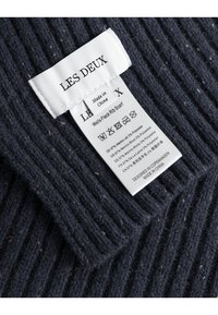 Mörk marinblå ribbad scarf i ull och polyesterblandning med inslag, med en vit skötsellapp som visar varumärke och materialinformation.