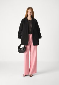Černý oversized blazer, průsvitný černý krajkový top, růžové široké kalhoty a černá zakřivená kabelka. Hladké textury, neutrální tóny.