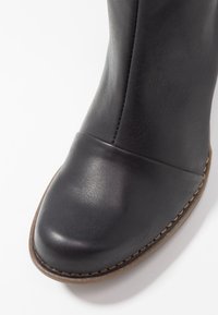 Black leather boot with a smooth finish and rounded toe. Features a contrast stitching along the sole and a tall shaft for coverage.