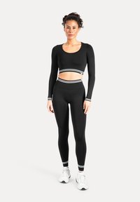 Sort træningssæt med langærmet top og højtaljede leggings. Det har stribede detaljer ved sømmen og ved håndleddene. Glat, strækbart stof.