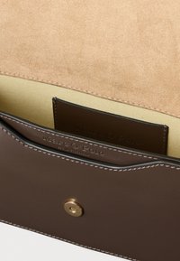 Denarnica iz rjavega usnja z zlato zaponko; ima kavčukasto svetlo rjavo preklopno zanko in bež notranjost, ki prikazuje režo za kartico z blagovno znamko.