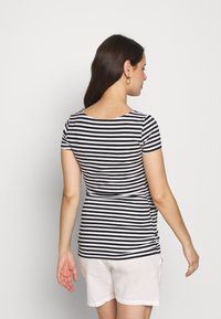 Top de manga curta às riscas pretas e brancas, com gola arredondada, forma ajustada e tecido suave. Usado com calções de cor clara.