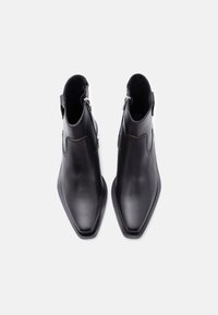 Ζευγάρι μαύρα δερμάτινα μποτάκια μέχρι τον αστράγαλο με μυτερά μπροστινά μέρη και πλευρικά φερμουάρ, σε λευκό φόντο, φωτογραφημένα από ψηλά.
