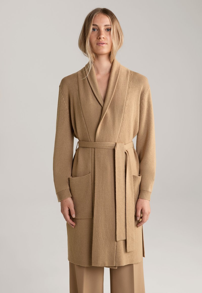 Beige gestrickte Strickjacke mit Schalkragen, langen Ärmeln, Bindegürtel und zwei Fronttaschen. Strukturiertes Gewebe mit glatter Oberfläche.