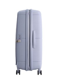 Hellgrauer Hartschalentrolley mit vier Rädern, seitlichem Griff und integriertem Zahlenschloss vor einem weißen Hintergrund.