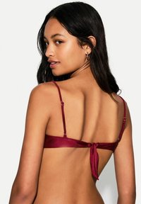 Burgundy satin bra with thin adjustable straps, a tied back feature, and a smooth texture. Minimalistic design with subtle shine.