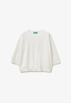 Biała skrócona bluza z szerokimi rękawami do łokcia i ściągaczami przy dekolcie, mankietach oraz u dołu, z zieloną metką marki wewnątrz kołnierza.